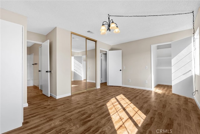 unfurnished bedroom featuring dark wood-type flooring, an inviting chandelier, and a textured ceiling