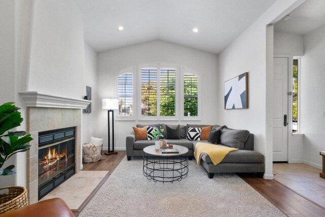 living room featuring vaulted ceiling, a tile fireplace, and hardwood / wood-style floors