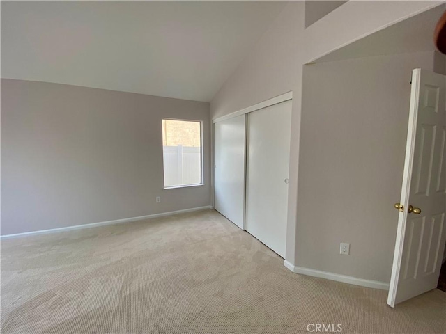 unfurnished bedroom featuring light carpet, a closet, and lofted ceiling