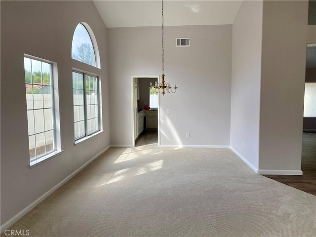 carpeted empty room featuring high vaulted ceiling and a notable chandelier