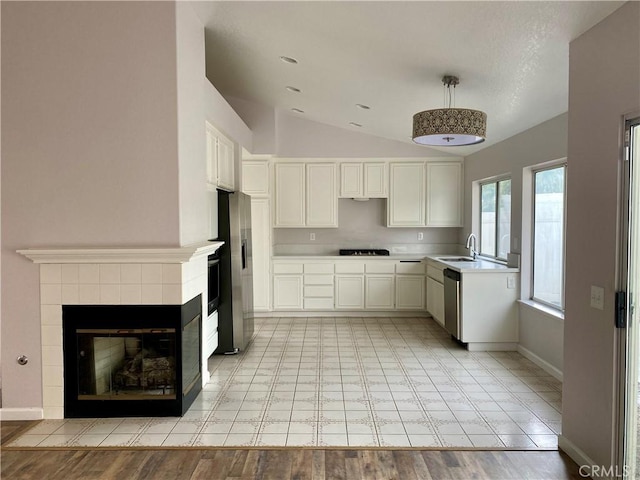 kitchen featuring white cabinetry, appliances with stainless steel finishes, a tiled fireplace, lofted ceiling, and sink