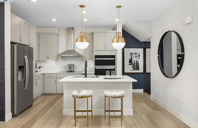 kitchen featuring pendant lighting, a center island with sink, wall chimney exhaust hood, double oven, and stainless steel fridge