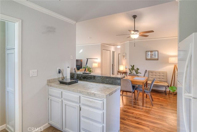 kitchen featuring white fridge, kitchen peninsula, ceiling fan, light wood-type flooring, and ornamental molding