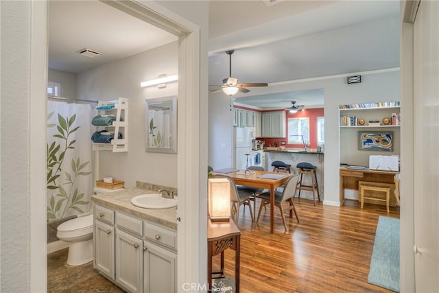 bathroom with wood-type flooring, vanity, toilet, walk in shower, and ceiling fan