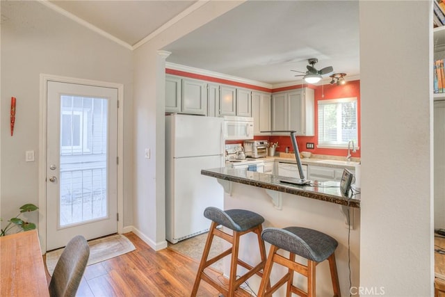 kitchen featuring ceiling fan, a breakfast bar area, white appliances, ornamental molding, and light hardwood / wood-style flooring