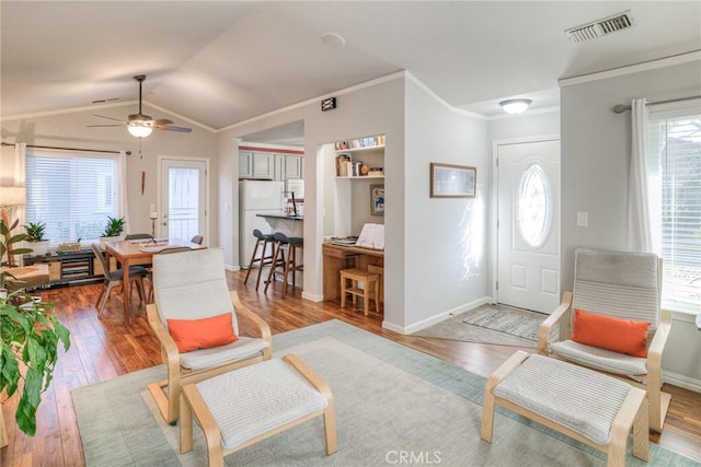 living room featuring ceiling fan, wood-type flooring, ornamental molding, and vaulted ceiling