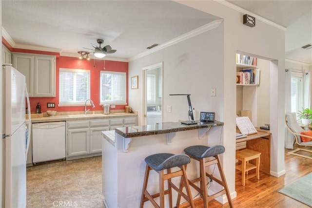 kitchen with sink, white appliances, crown molding, light wood-type flooring, and a kitchen breakfast bar