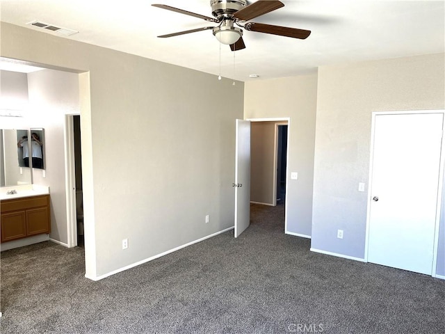 unfurnished bedroom with ceiling fan, ensuite bathroom, and dark colored carpet