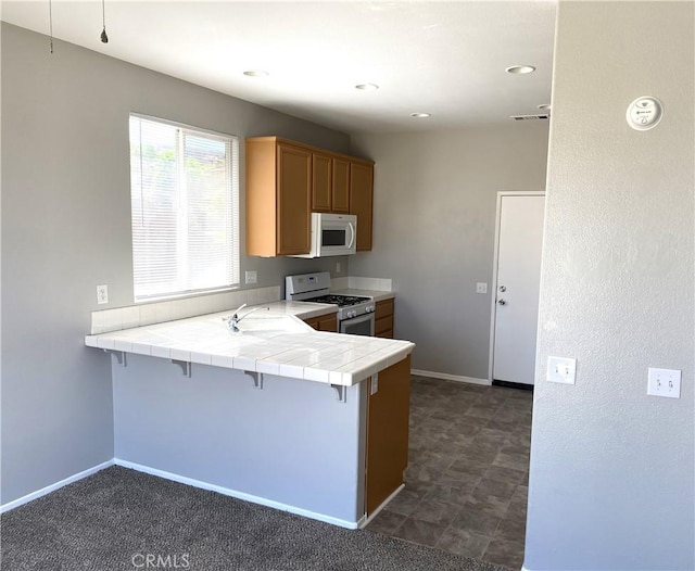 kitchen featuring kitchen peninsula, a breakfast bar area, tile counters, white appliances, and sink