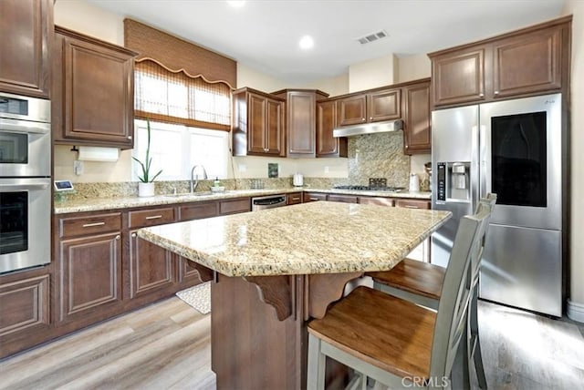 kitchen featuring light hardwood / wood-style floors, a breakfast bar area, appliances with stainless steel finishes, a center island, and sink