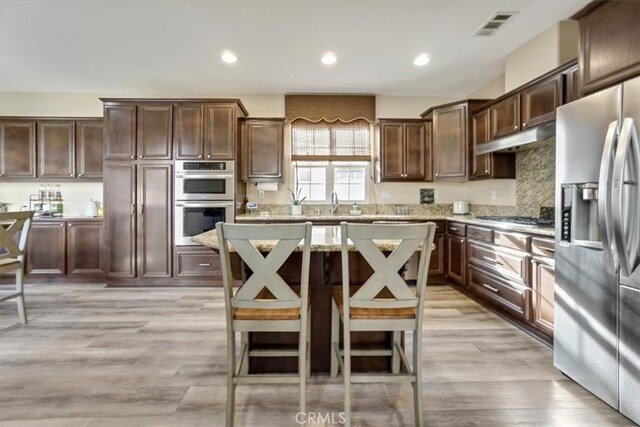 kitchen featuring dark brown cabinetry, a center island, stainless steel appliances, light hardwood / wood-style floors, and a kitchen breakfast bar