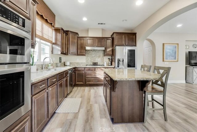 kitchen featuring a kitchen island, stainless steel appliances, backsplash, light hardwood / wood-style flooring, and a breakfast bar area