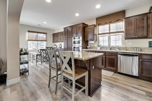 kitchen with stainless steel appliances, a center island, light stone countertops, light hardwood / wood-style flooring, and sink