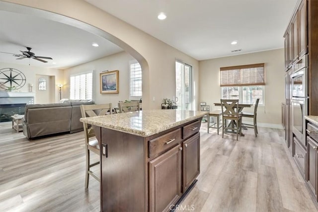 kitchen with light hardwood / wood-style floors, a breakfast bar area, ceiling fan, light stone countertops, and a center island