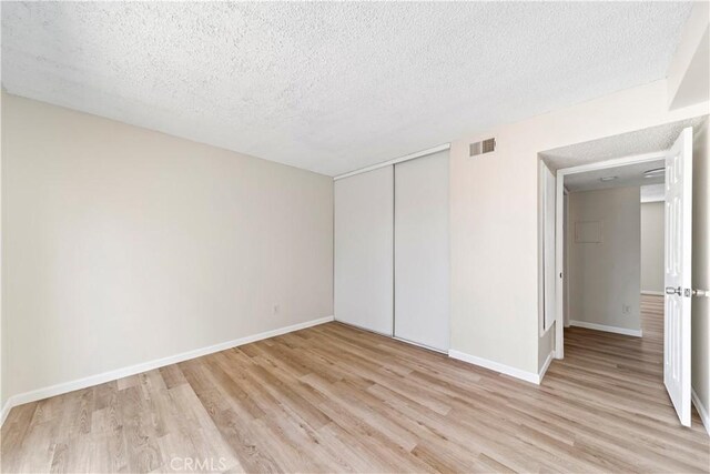 unfurnished bedroom featuring a closet, a textured ceiling, and light hardwood / wood-style flooring