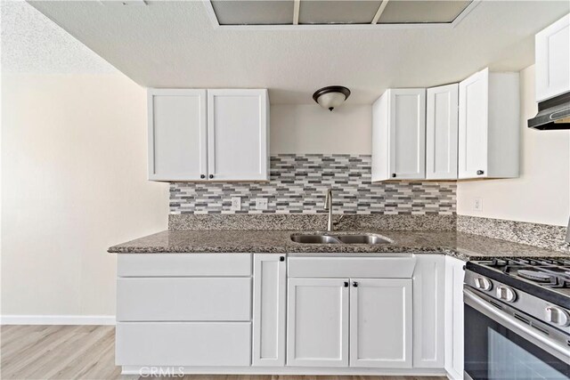 kitchen featuring white cabinets, tasteful backsplash, dark stone countertops, sink, and stainless steel range with gas stovetop