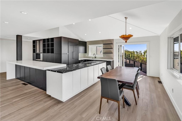 kitchen with light hardwood / wood-style floors, kitchen peninsula, lofted ceiling, hanging light fixtures, and sink