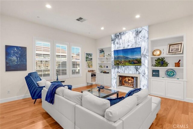 living room featuring built in shelves, light hardwood / wood-style flooring, and a large fireplace