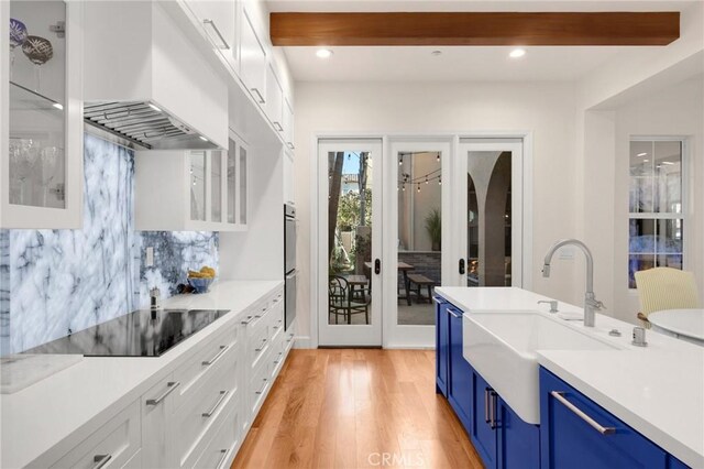 kitchen with sink, premium range hood, white cabinets, blue cabinets, and black electric cooktop