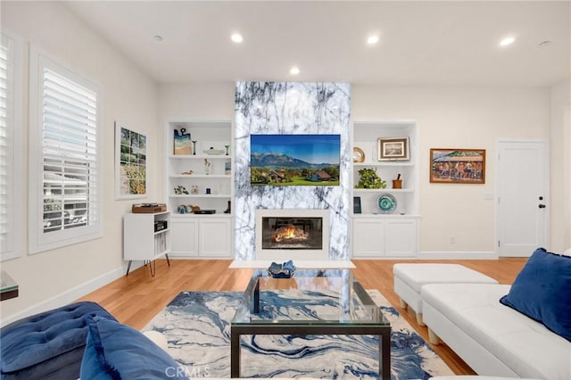 living room featuring built in shelves, light wood-type flooring, and a large fireplace