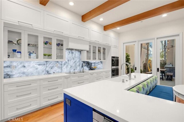 kitchen featuring double oven, sink, white cabinets, black electric stovetop, and beamed ceiling