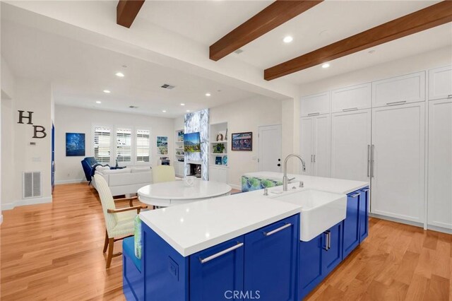 kitchen featuring beamed ceiling, sink, light wood-type flooring, a center island with sink, and blue cabinets