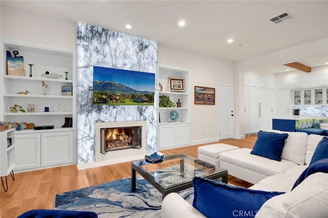 living room with built in shelves, light hardwood / wood-style floors, and a fireplace