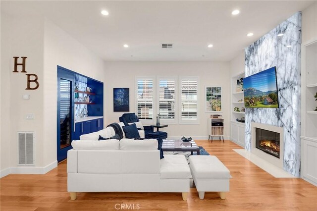 living room featuring light wood-type flooring, built in shelves, and a high end fireplace