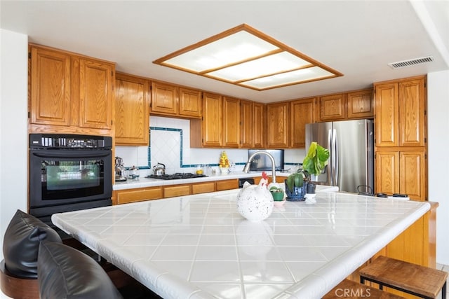 kitchen featuring oven, tile countertops, stainless steel fridge, and a kitchen breakfast bar