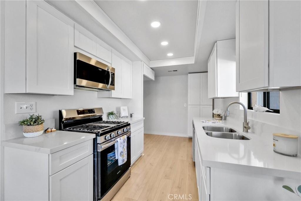 kitchen featuring stainless steel appliances, a tray ceiling, white cabinets, light hardwood / wood-style flooring, and sink