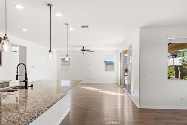 kitchen featuring ceiling fan, pendant lighting, light stone counters, and sink