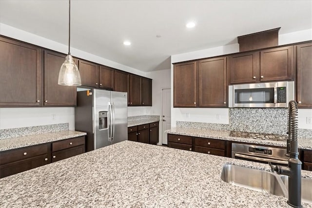 kitchen with pendant lighting, sink, light stone countertops, stainless steel appliances, and dark brown cabinets