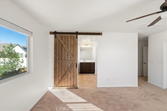 interior space with ensuite bath, a barn door, ceiling fan, and light colored carpet