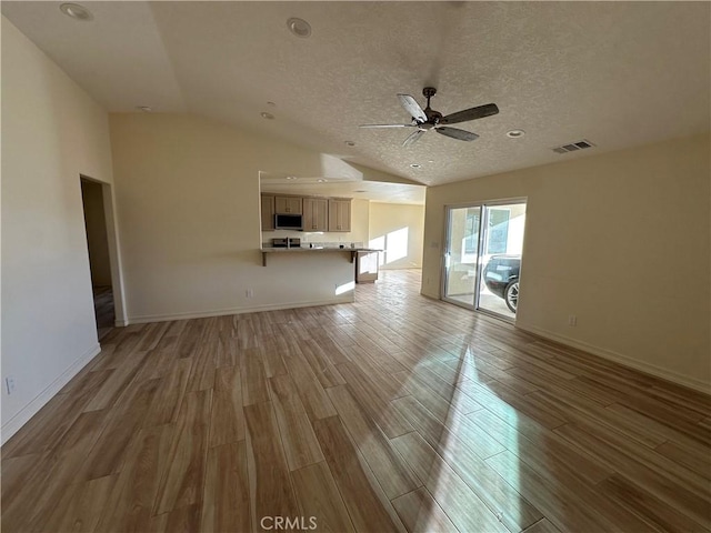 unfurnished living room with ceiling fan, vaulted ceiling, a textured ceiling, and light hardwood / wood-style floors