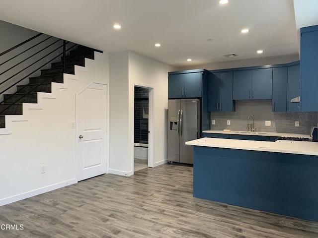 kitchen with light wood-type flooring, blue cabinetry, stainless steel fridge, and sink