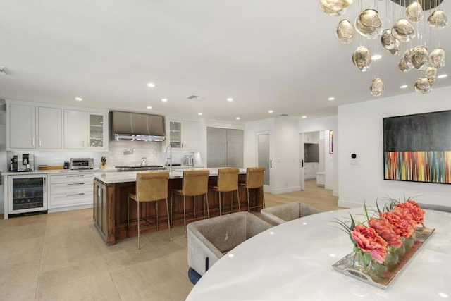 kitchen featuring wine cooler, a kitchen bar, an island with sink, and white cabinetry