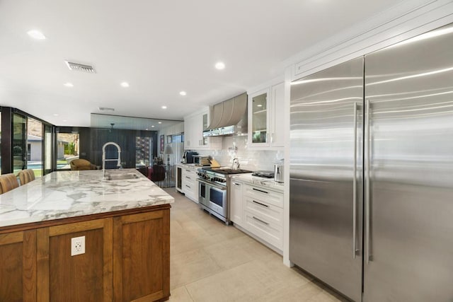 kitchen featuring white cabinets, a kitchen island with sink, wall chimney exhaust hood, and high end appliances