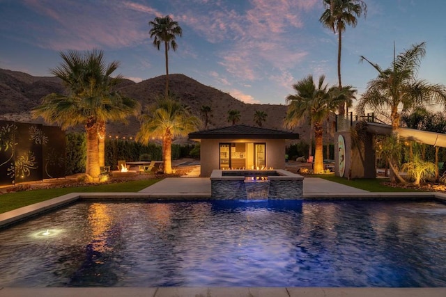 pool at dusk featuring an in ground hot tub, a mountain view, and a patio