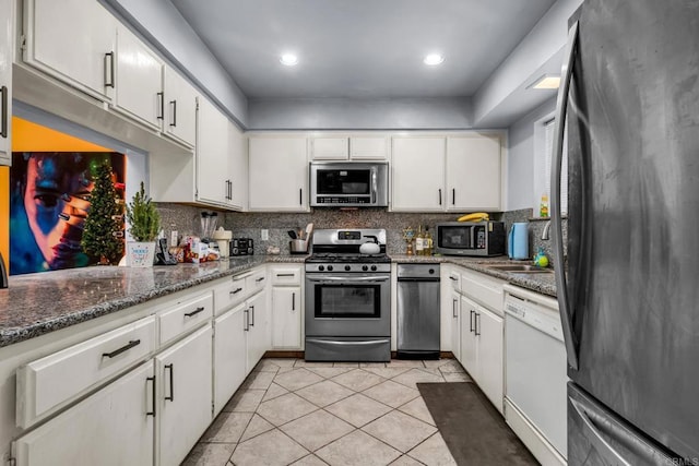 kitchen with backsplash, dark stone countertops, light tile patterned floors, stainless steel appliances, and white cabinets