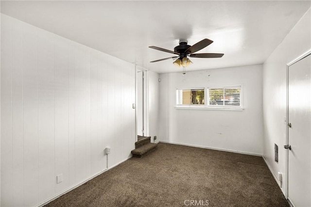 unfurnished room with ceiling fan and dark colored carpet