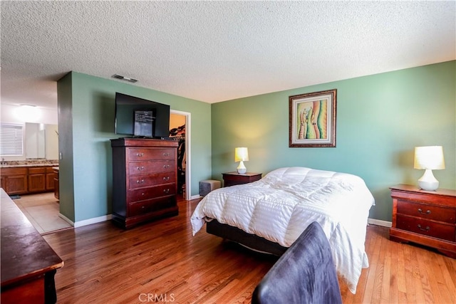 bedroom featuring ensuite bath, light hardwood / wood-style flooring, a textured ceiling, a walk in closet, and a closet