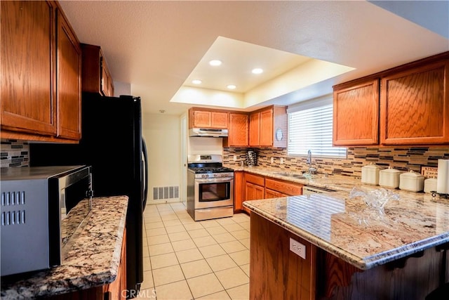 kitchen featuring stainless steel appliances, sink, kitchen peninsula, a raised ceiling, and light stone counters