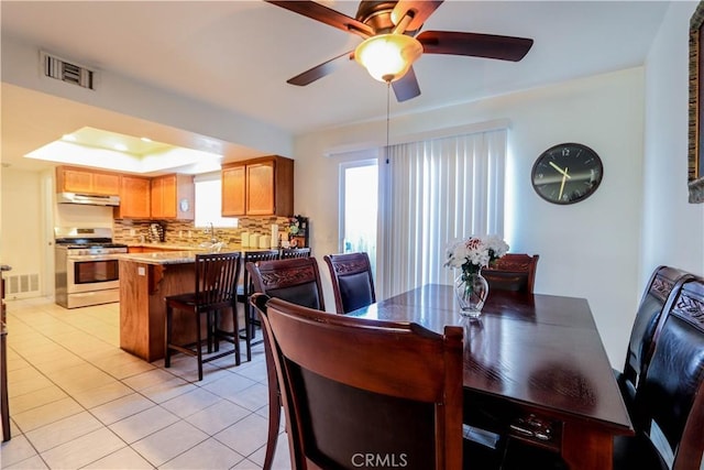 tiled dining space featuring ceiling fan and a raised ceiling