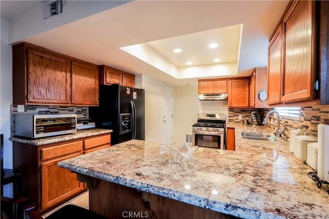 kitchen featuring sink, black fridge, kitchen peninsula, gas range, and a tray ceiling