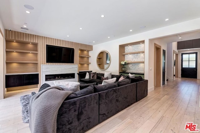 living room with light hardwood / wood-style floors, built in features, and a premium fireplace