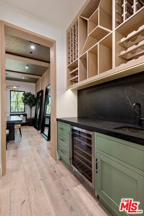 bar featuring light wood-type flooring, sink, wine cooler, and green cabinetry