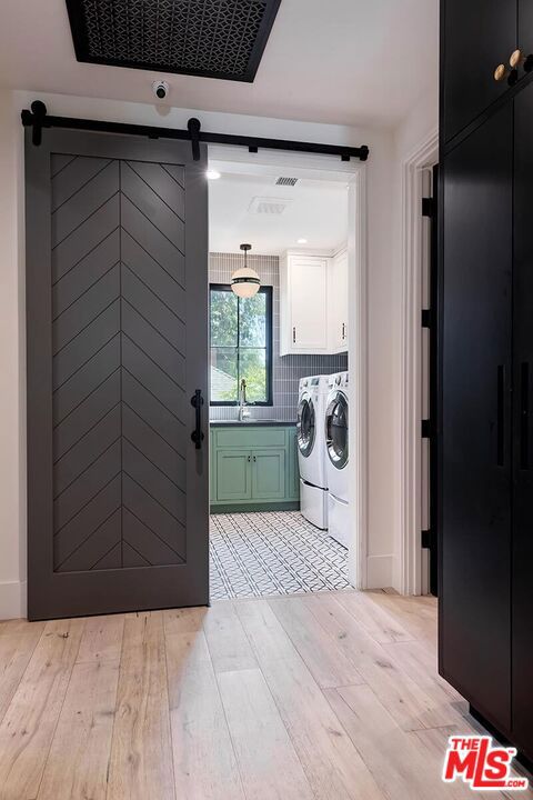 laundry area featuring light hardwood / wood-style floors, a barn door, washing machine and dryer, cabinets, and sink