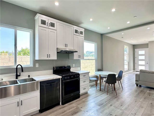 kitchen with light stone countertops, black appliances, white cabinetry, light hardwood / wood-style floors, and sink