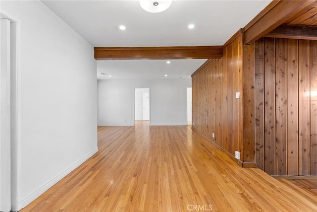 spare room with light wood-type flooring, beam ceiling, and wooden walls