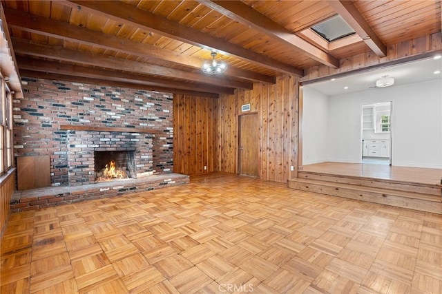 unfurnished living room featuring light parquet floors, a skylight, wood walls, a fireplace, and beam ceiling